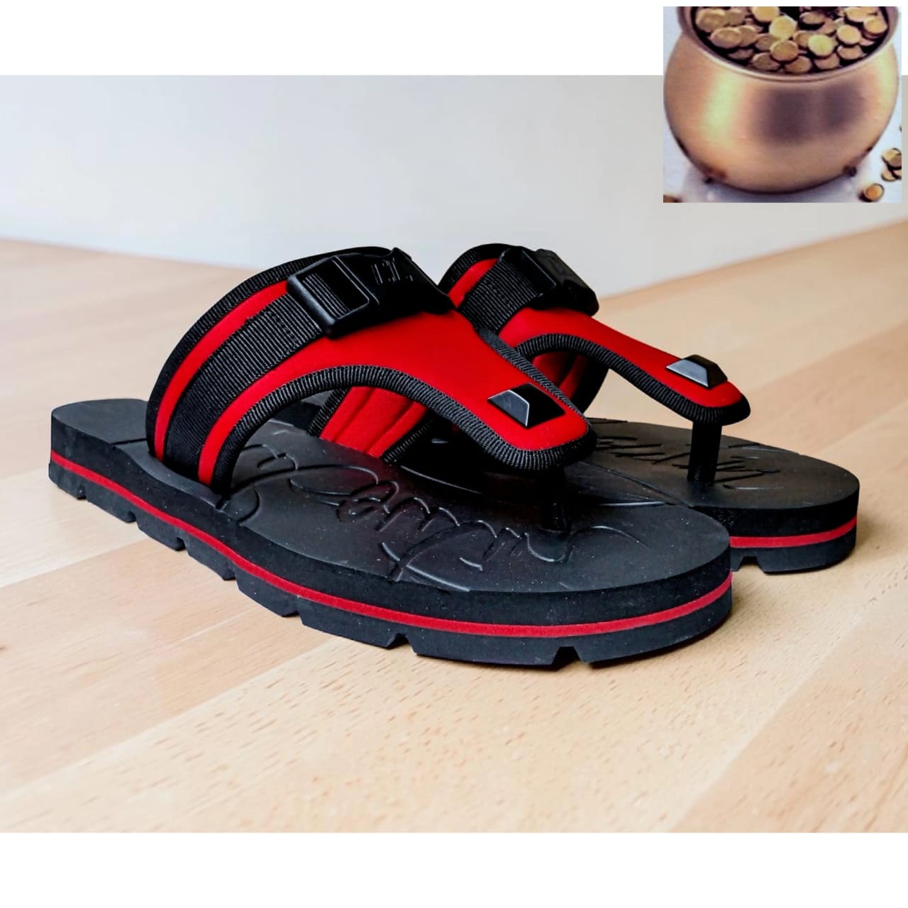 Black and red tactical padded flip sandal with neoprene straps, buckle hardware, pyramid stud accents, and chunky black rubber sole with red midsole stripe — displayed on a wooden floor