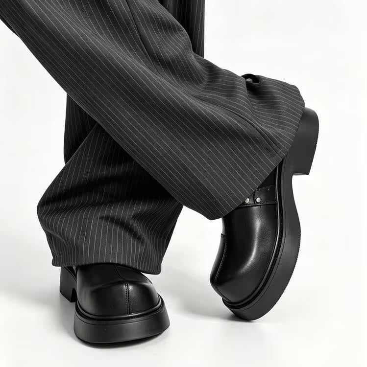 Black leather platform loafers with a glossy finish, shown on a model wearing black pinstripe wide-leg trousers against a white studio background.