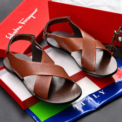 A pair of black leather criss-cross strappy sandals with adjustable ankle straps, displayed on a white surface next to a yellow beaded bracelet.