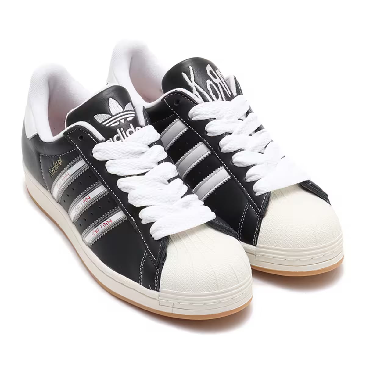 Adidas Superstar x Korn Est. 1994 collaboration sneakers in black leather with silver stripes, off-white shell toe, chunky white laces, and gum sole — Swingdot Luxe