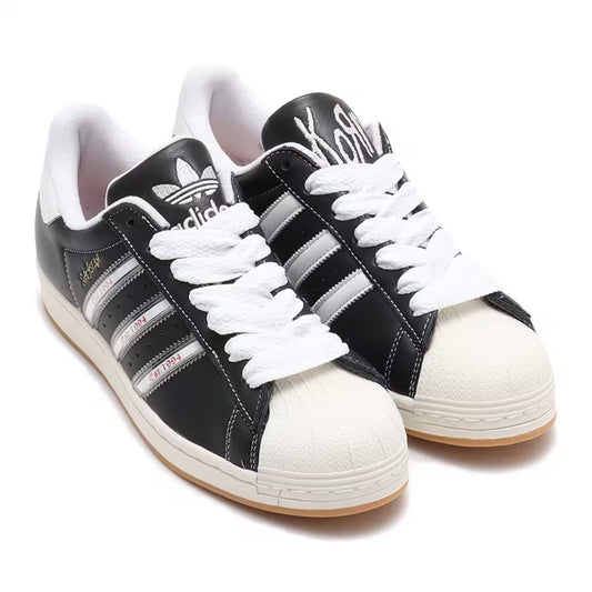 Adidas Superstar x Korn Est. 1994 collaboration sneakers in black leather with silver stripes, off-white shell toe, chunky white laces, and gum sole — Swingdot Luxe