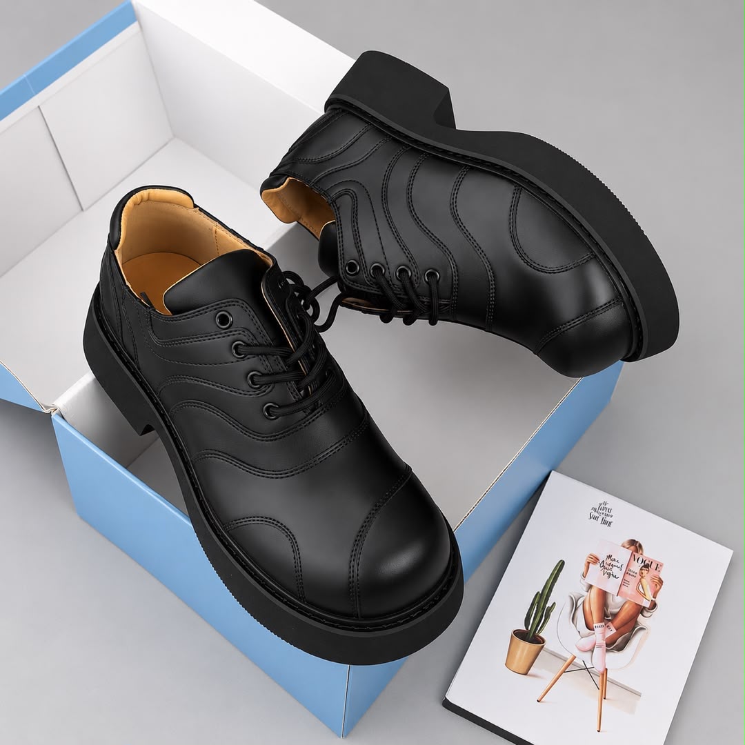 Pair of black panelled men's lace-up shoes with tonal stitched detailing and a substantial black sole in a shoebox