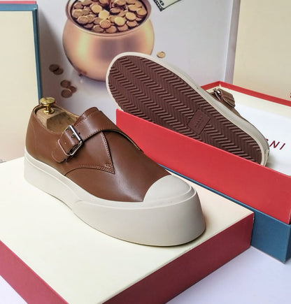 Tan calfskin leather monk strap platform sneaker with polished silver buckle, white cap toe, and thick white herringbone rubber sole — side and sole view on a red luxury shoe box