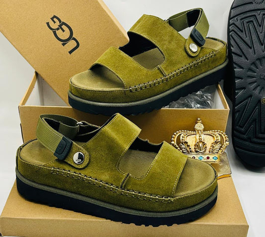 UGG Goldenstar olive moss green suede double-strap sandals with UGG logo buckle ankle strap, silver medallion stud toe detail, tonal espadrille midsole stitching, and black rubber outsole on UGG kraft box — 100% authentic men's luxury sandals