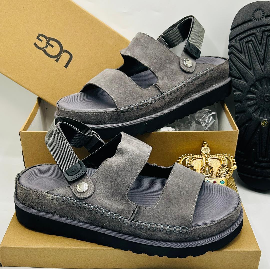 UGG Goldenstar charcoal grey suede double-strap sandals with UGG logo buckle ankle strap, silver medallion stud toe detail, tonal grey espadrille midsole stitching, and black rubber outsole on UGG kraft box — 100% authentic men's luxury sandals