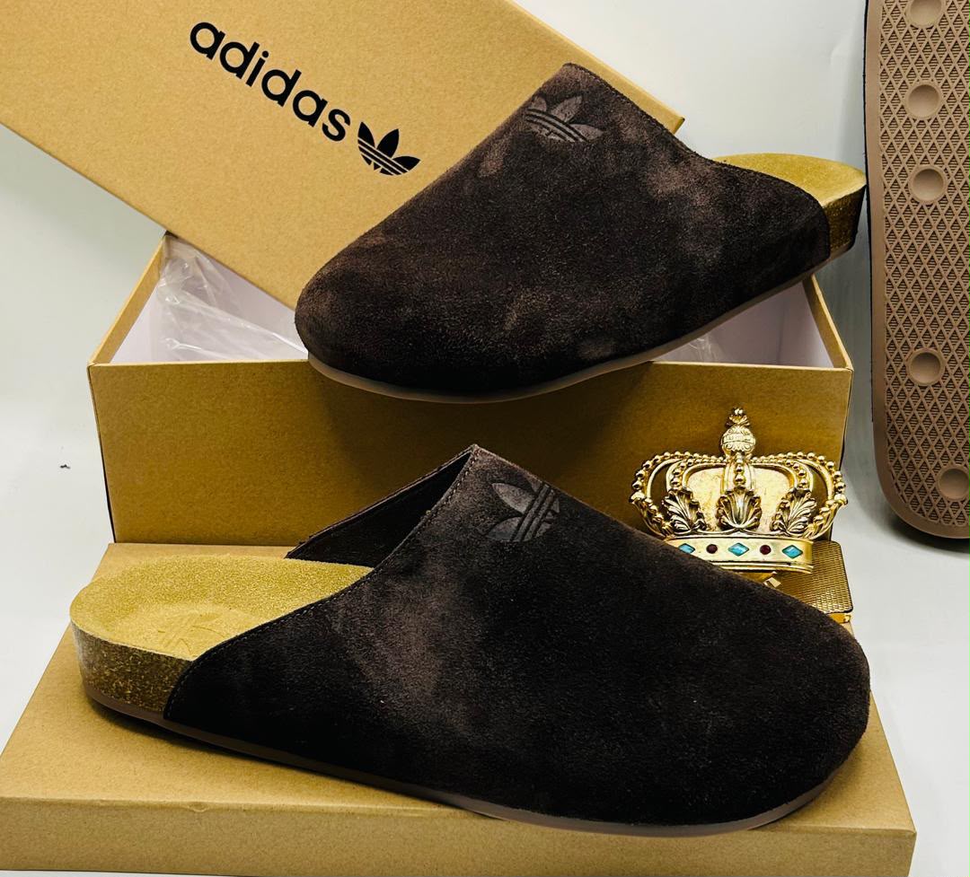 Adidas Originals dark brown suede closed-toe mule clogs with embossed Trefoil logo, natural cork-effect gold footbed, and textured rubber outsole on Adidas gold kraft box — 100% authentic men's luxury footwear