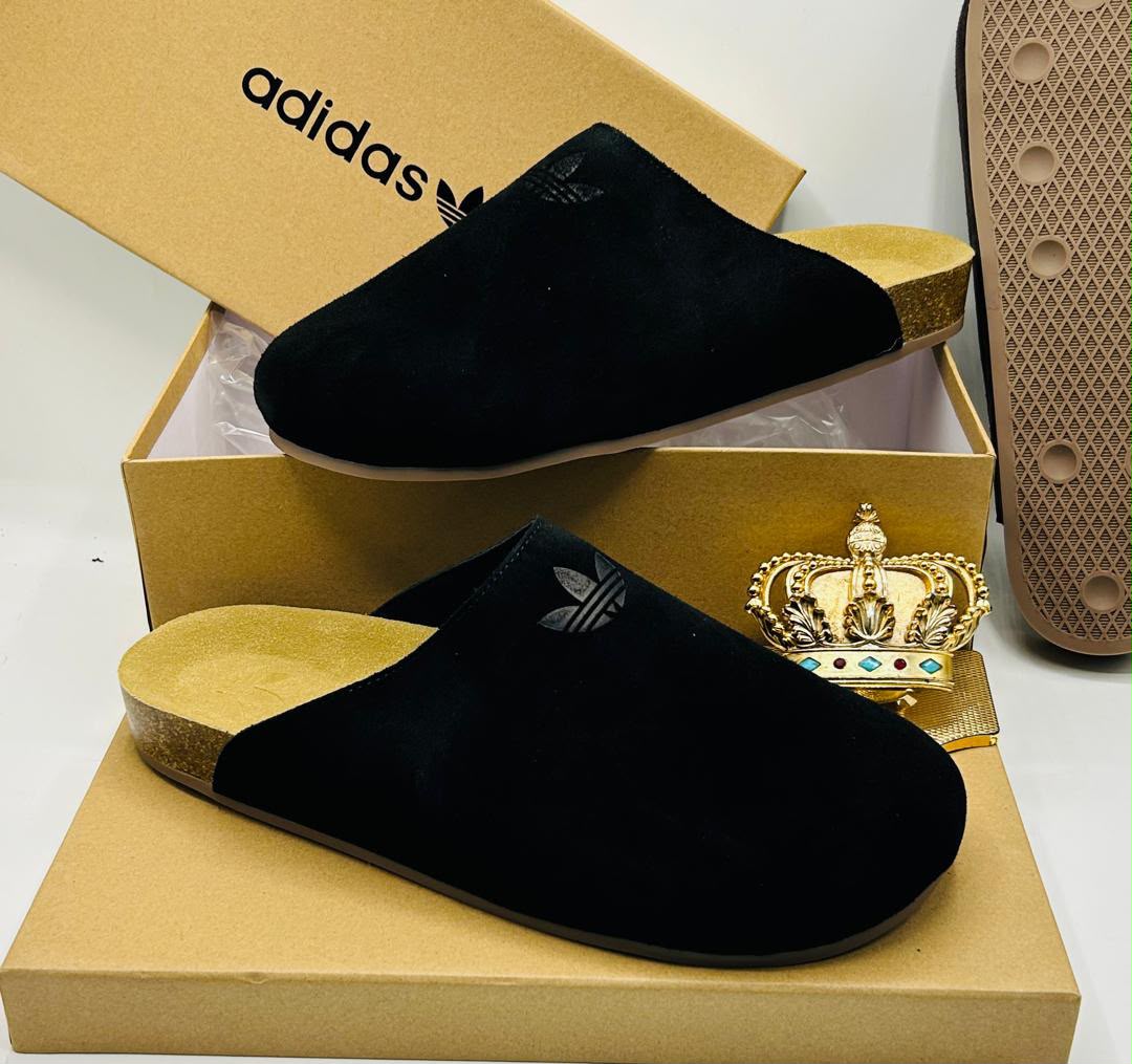Adidas Originals black suede closed-toe mule clogs with embossed tonal Trefoil logo, natural cork-effect gold footbed, and textured rubber outsole on Adidas gold kraft box — 100% authentic men's luxury footwear