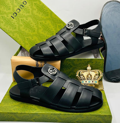 Gucci black leather Interlocking G fisherman sandals with silver GG logo medallion on toe strap, woven leather cage upper, adjustable ankle buckle strap, and black rubber sole on Gucci green floral box — 100% authentic men's luxury sandals