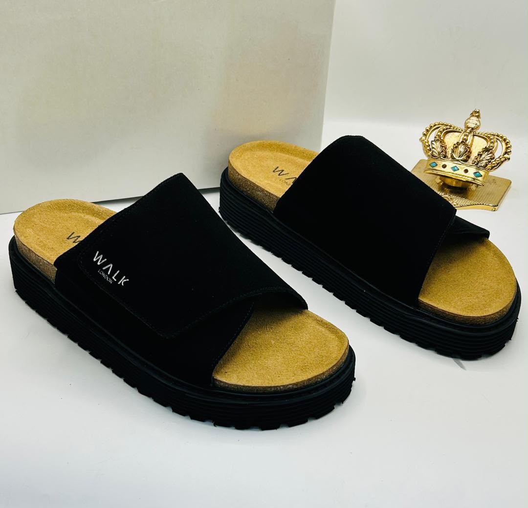 Walk London black suede wide single-strap platform slides with WALK LONDON embroidered wordmark in white, natural cork-effect tan footbed, and chunky black ridged rubber outsole on white box with gold crown prop — 100% authentic men's luxury slides