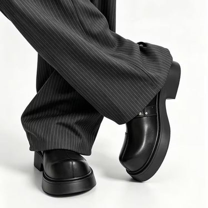 Black leather platform loafers with a glossy finish, shown on a model wearing black pinstripe wide-leg trousers against a white studio background.