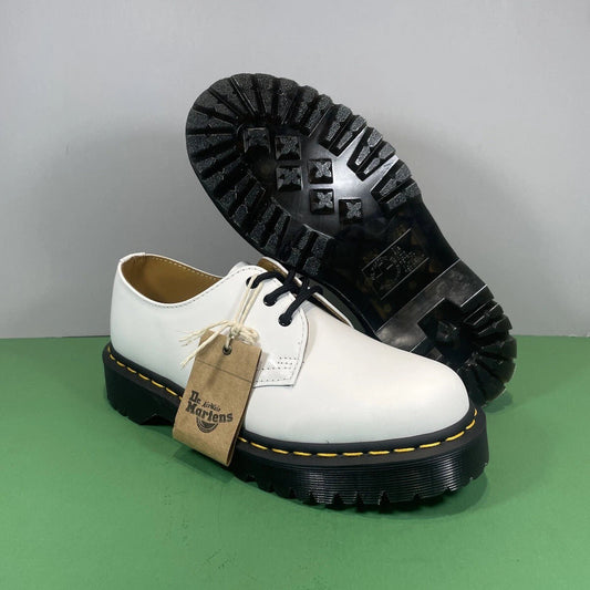 A pair of white Dr. Martens 1431 boots with black soles, one standing upright and the other tilted to show the treaded outsole.